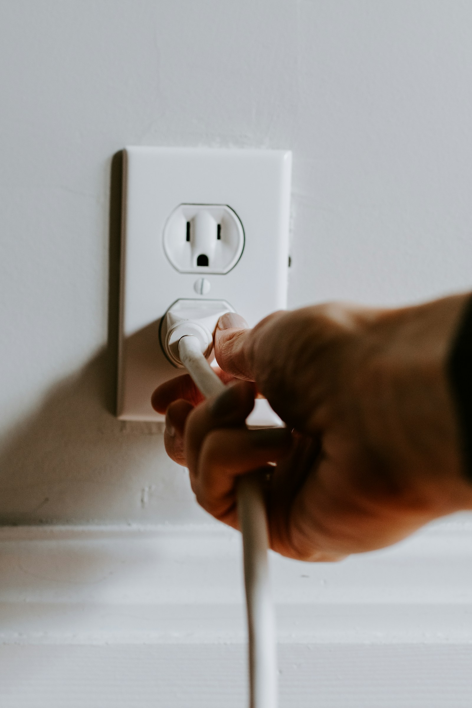 A hand plugging a power cable into a wall outlet